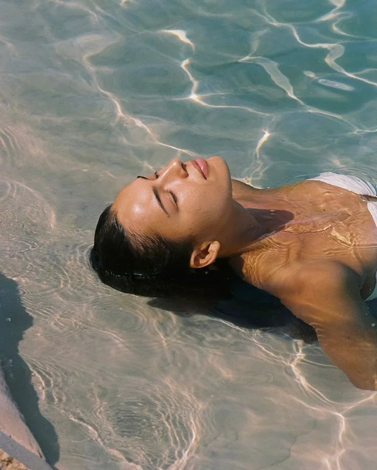 Jonge vrouw die relaxed achterover ligt in het water met haar ogen dicht